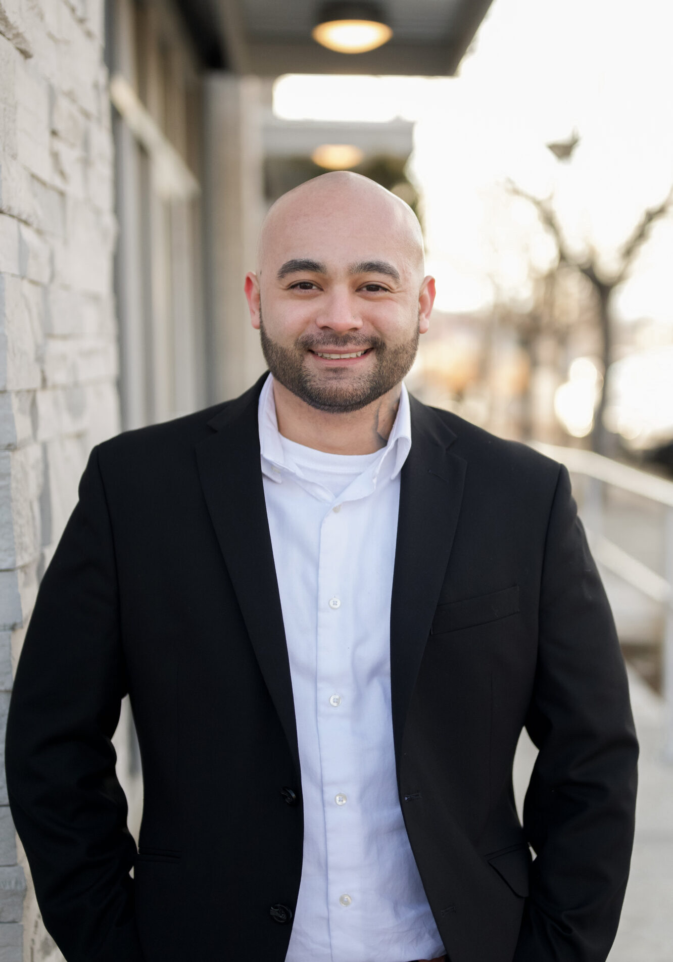 Smiling bald man in a black suit jacket and white shirt outdoors.